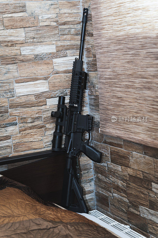 用于家庭防御的民用武器。一把ar - 15步枪，配有光学瞄准镜，靠近房间的墙壁。